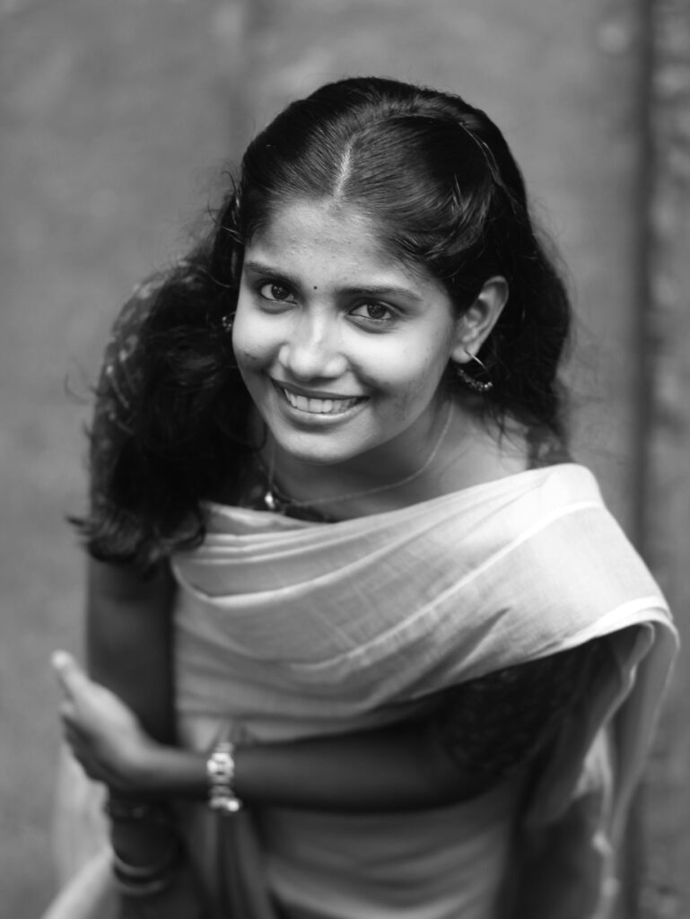 A black and white portrait of a smiling woman in traditional Indian attire.